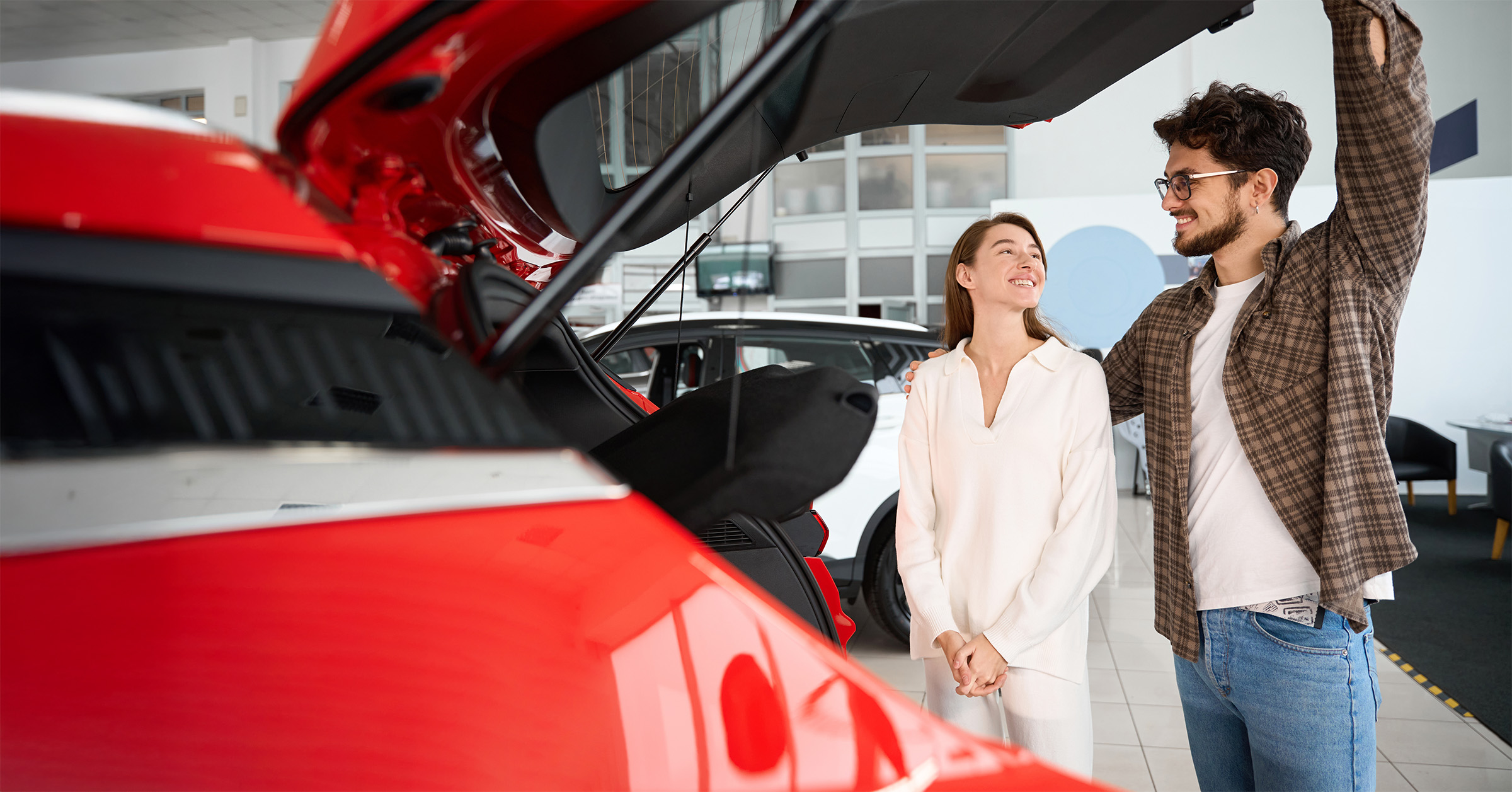 Mies- ja nainen katsomassa punaisen auton takakonttia autoliikeessä